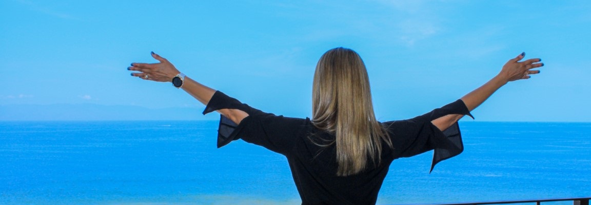 Image of Marilu holding wide arms towards the ocean